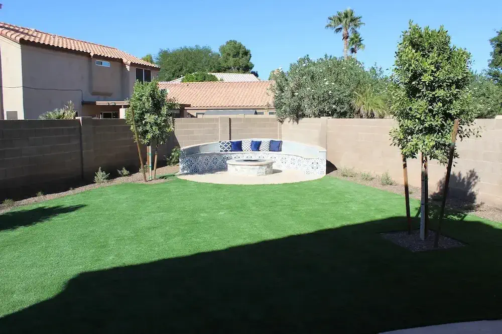 Image of a newly landcaped backyard with artificial turf, a flagstone fireplace patio, and desert tolerant plants